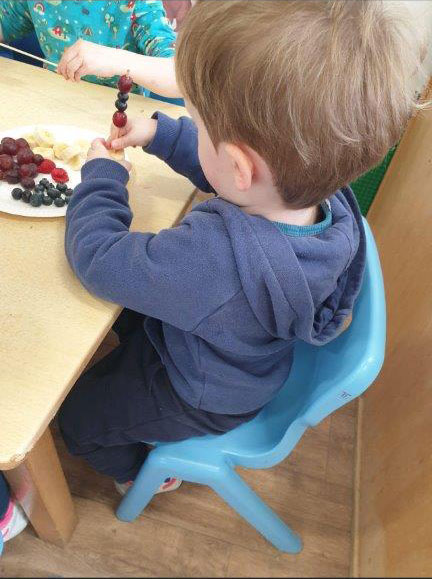 A child making a fruit skewer at the table